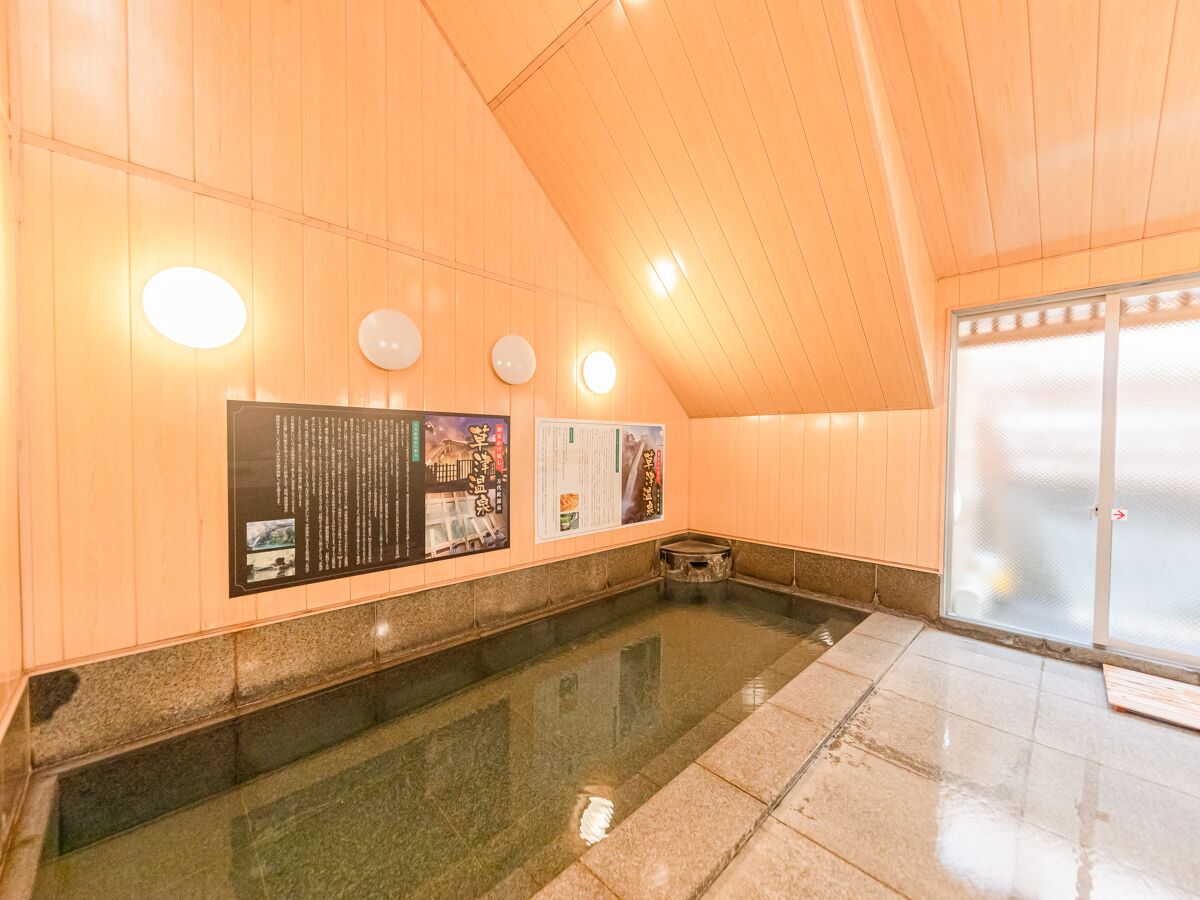 Un onsen japonais traditionnel, avec des murs en bois, une source d’eau chaude alimentée par des pierres et des panneaux d’information.