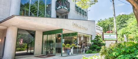 The exterior of Livemax Resort with a modern glass facade, a covered entrance, and lush greenery around.