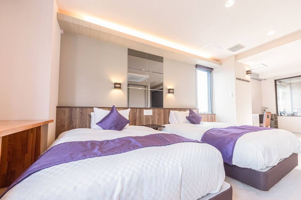 A modern hotel room with two beds, a large mirror, and a wooden headboard.