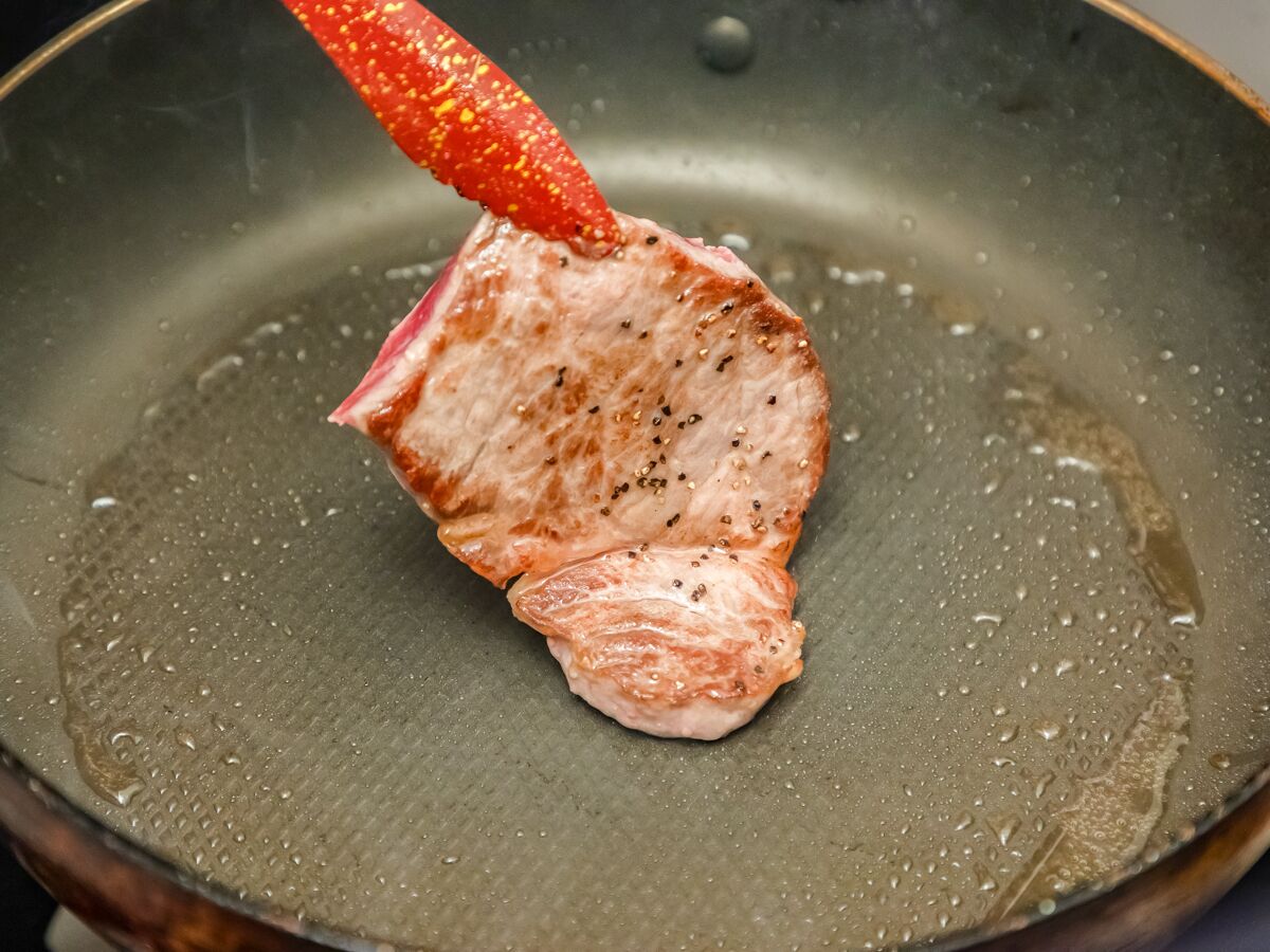 A raw piece of meat being cooked in a pan.