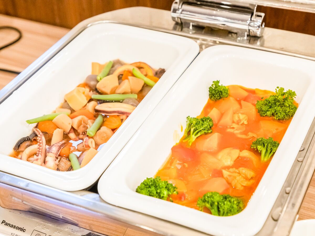Two white rectangular dishes with food, one with octopus and vegetables, and the other with a tomato-based soup and broccoli.