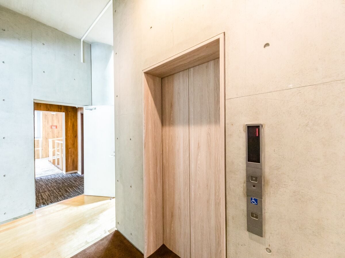 A modern elevator with a digital display, a wooden door, and a concrete wall.