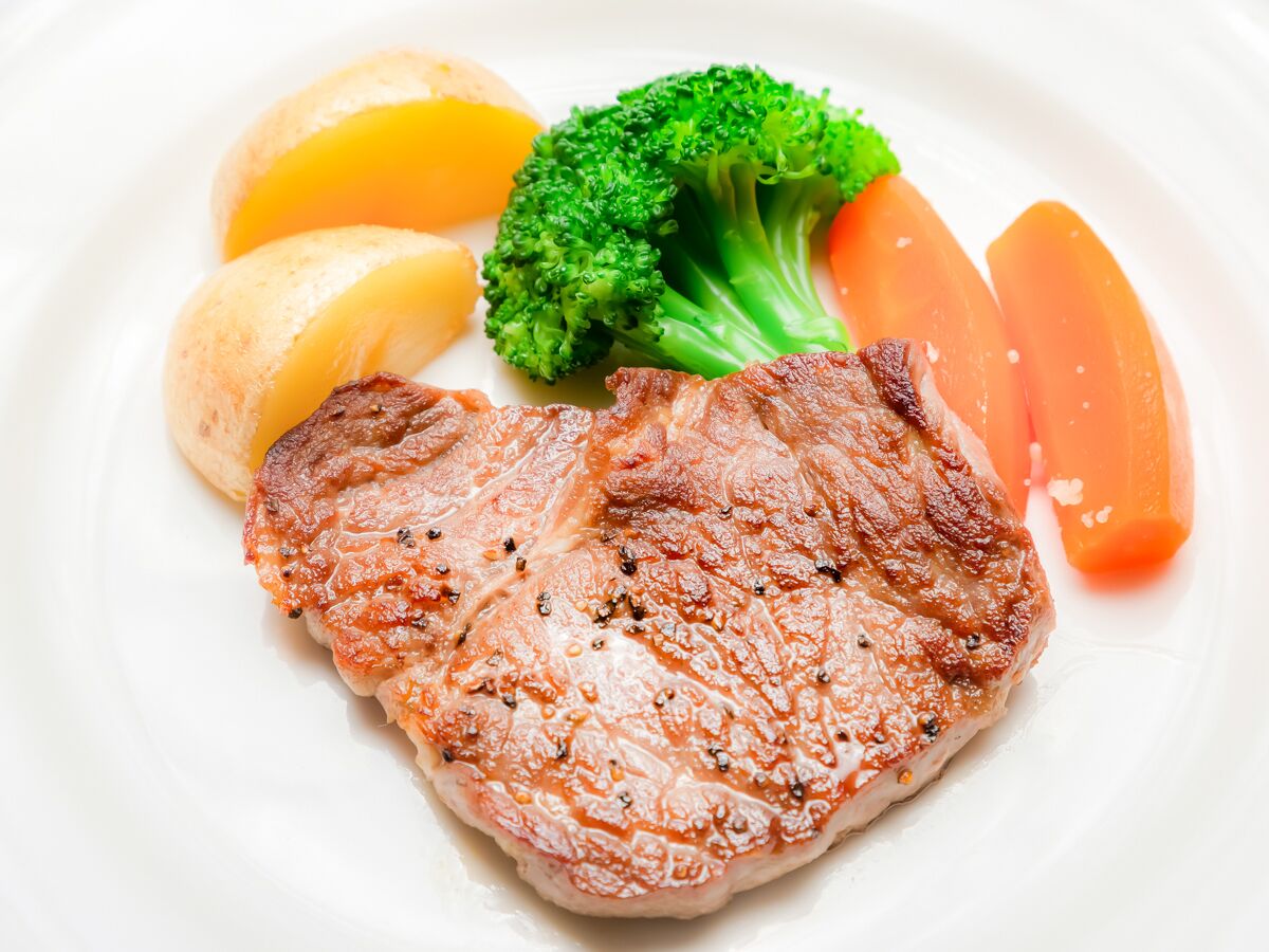 A plate with a grilled steak, broccoli, lemon slices, and carrots.