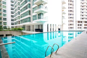 A modern indoor swimming pool with clear blue water, surrounded by high-rise residential buildings with balconies. - Regalia Residence by Cobnb (Kuala Lumpur)