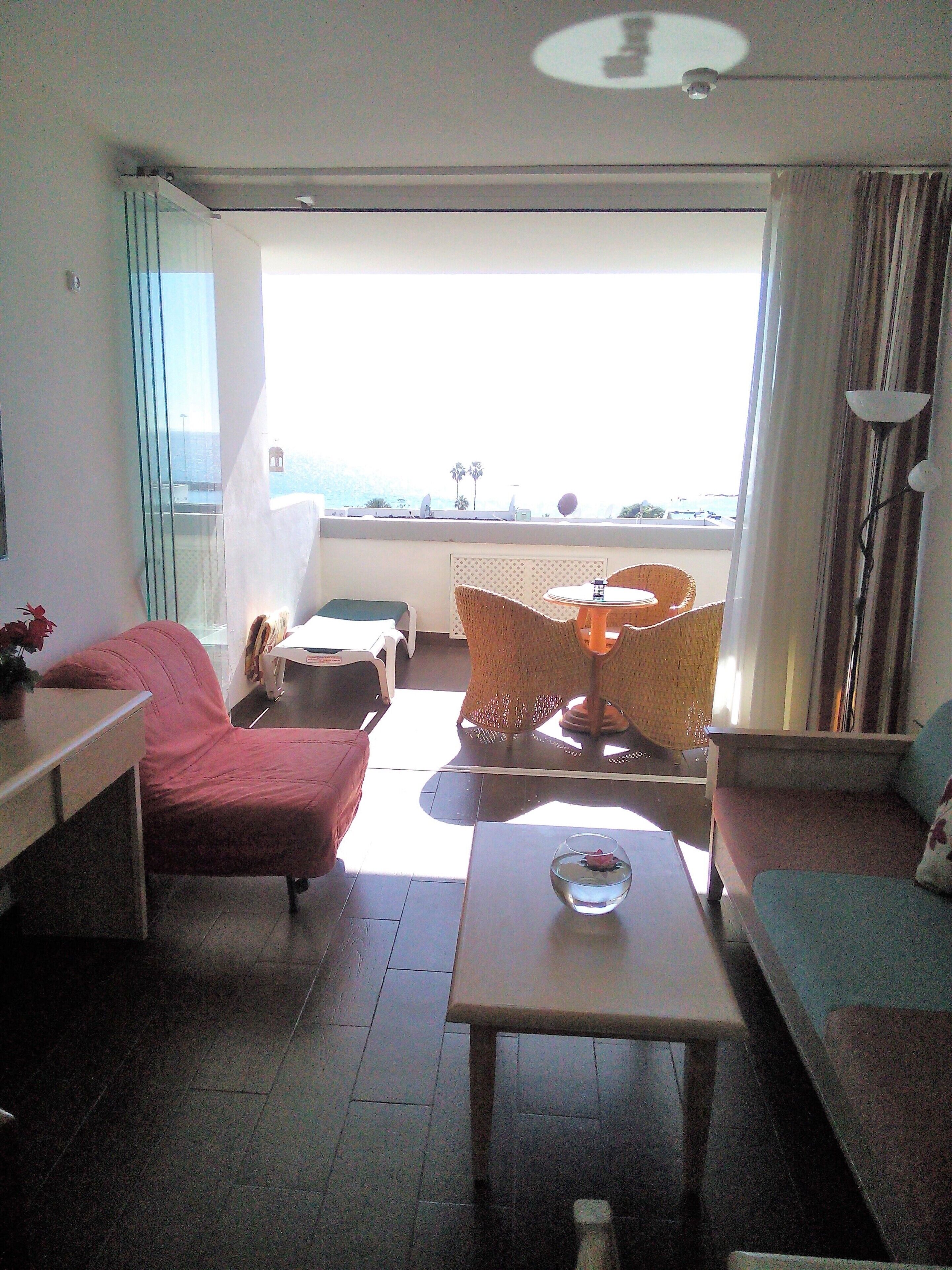 A hotel room with a balcony, a sofa, a table, and a chair.