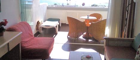A hotel room with a balcony, a sofa, a table, and a chair.