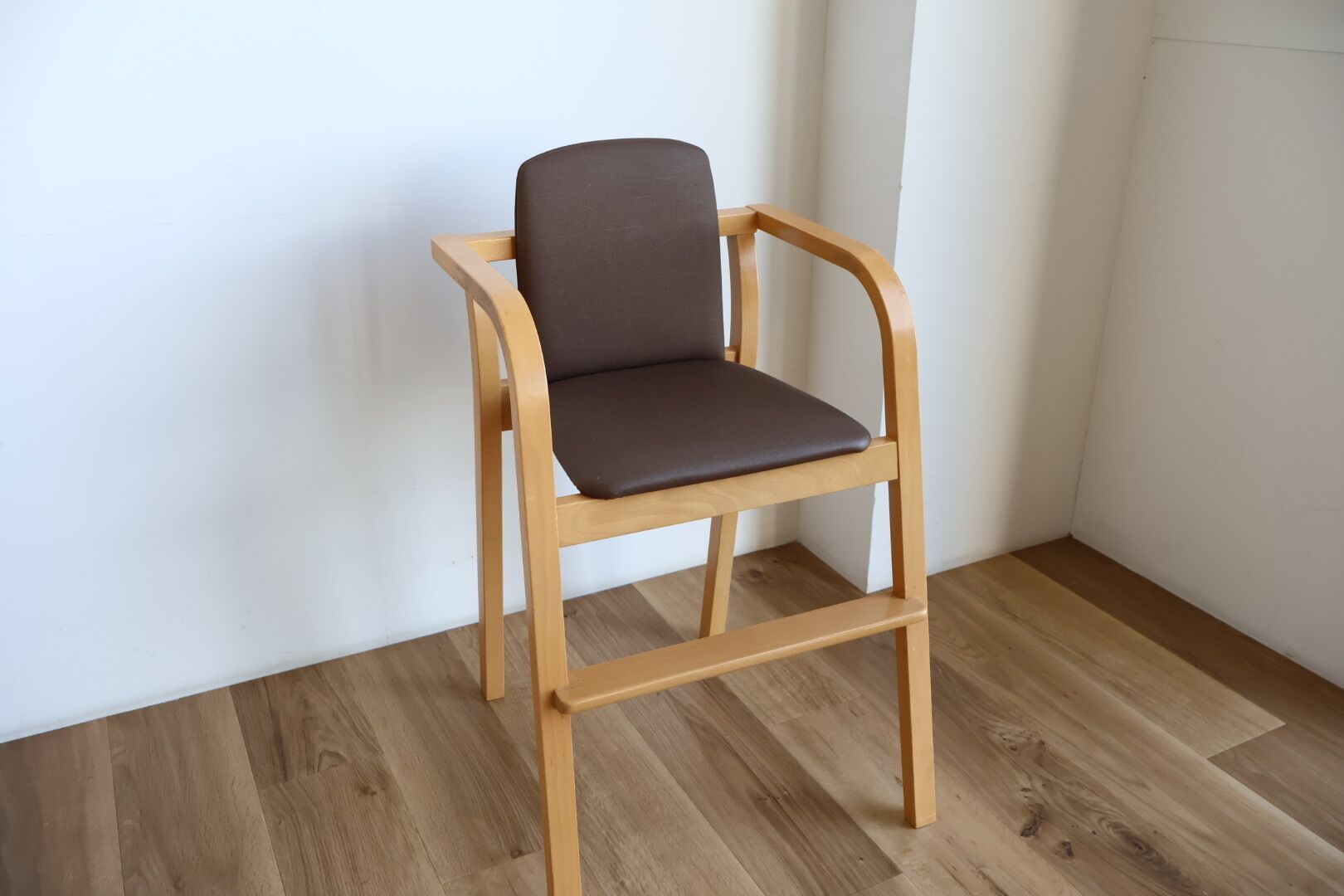A wooden chair with a dark cushion in a room with wooden flooring and white walls.