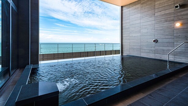 Une piscine intérieure moderne avec vue sur la mer, un plafond en bois et un sol carrelé.