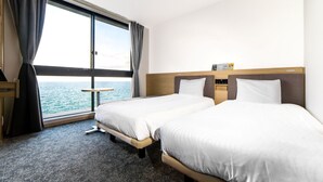 Une chambre d’hôtel avec deux lits, une petite table et vue sur la mer.