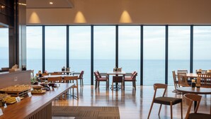 Un espace repas moderne doté de grandes fenêtres donnant sur la mer, de meubles en bois et d’un buffet.