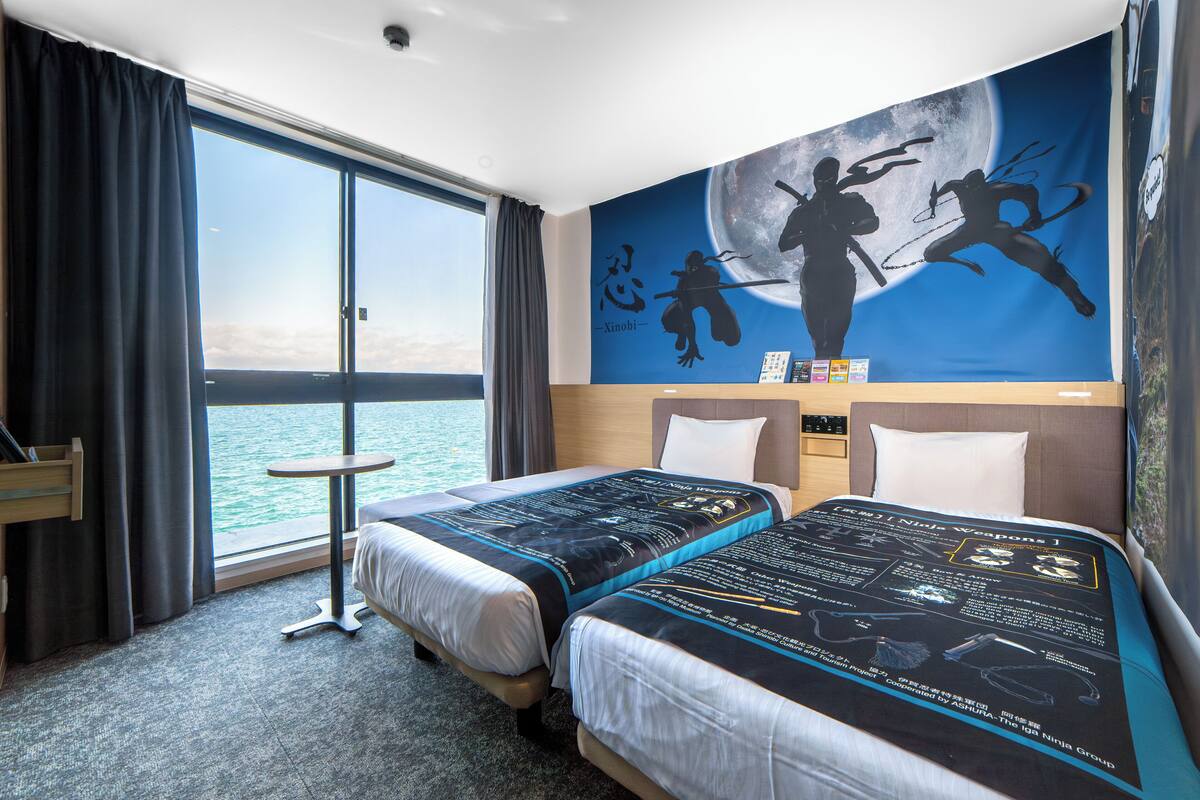 A hotel room with two beds, a view of the sea, and a mural on the wall.