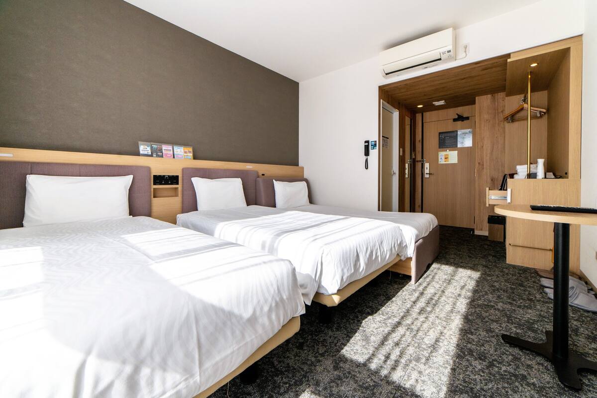 A hotel room with two beds, a desk, a chair, and a wardrobe.