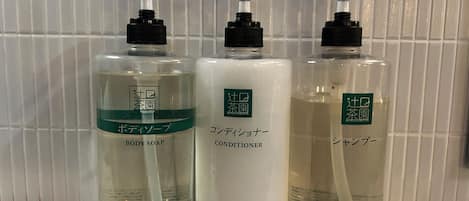 Three bottles of liquid products with pump dispensers, labeled in a foreign language, on a tiled shelf.
