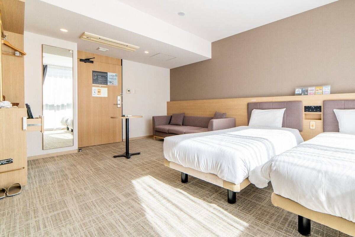 A hotel room with two beds, a sofa, a desk, and a mirror.