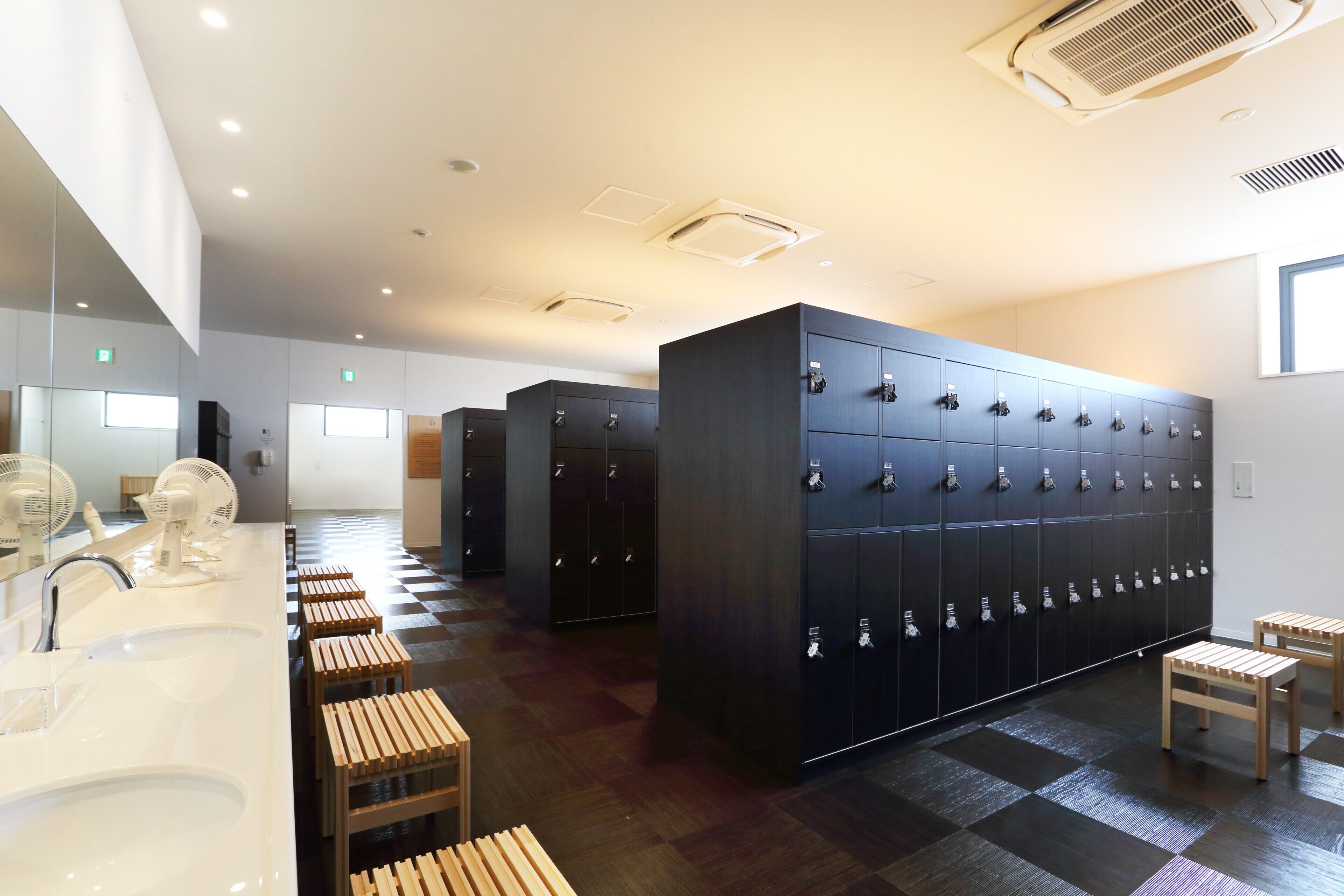 A modern bathroom with multiple lockers, wooden stools, and a large mirror.