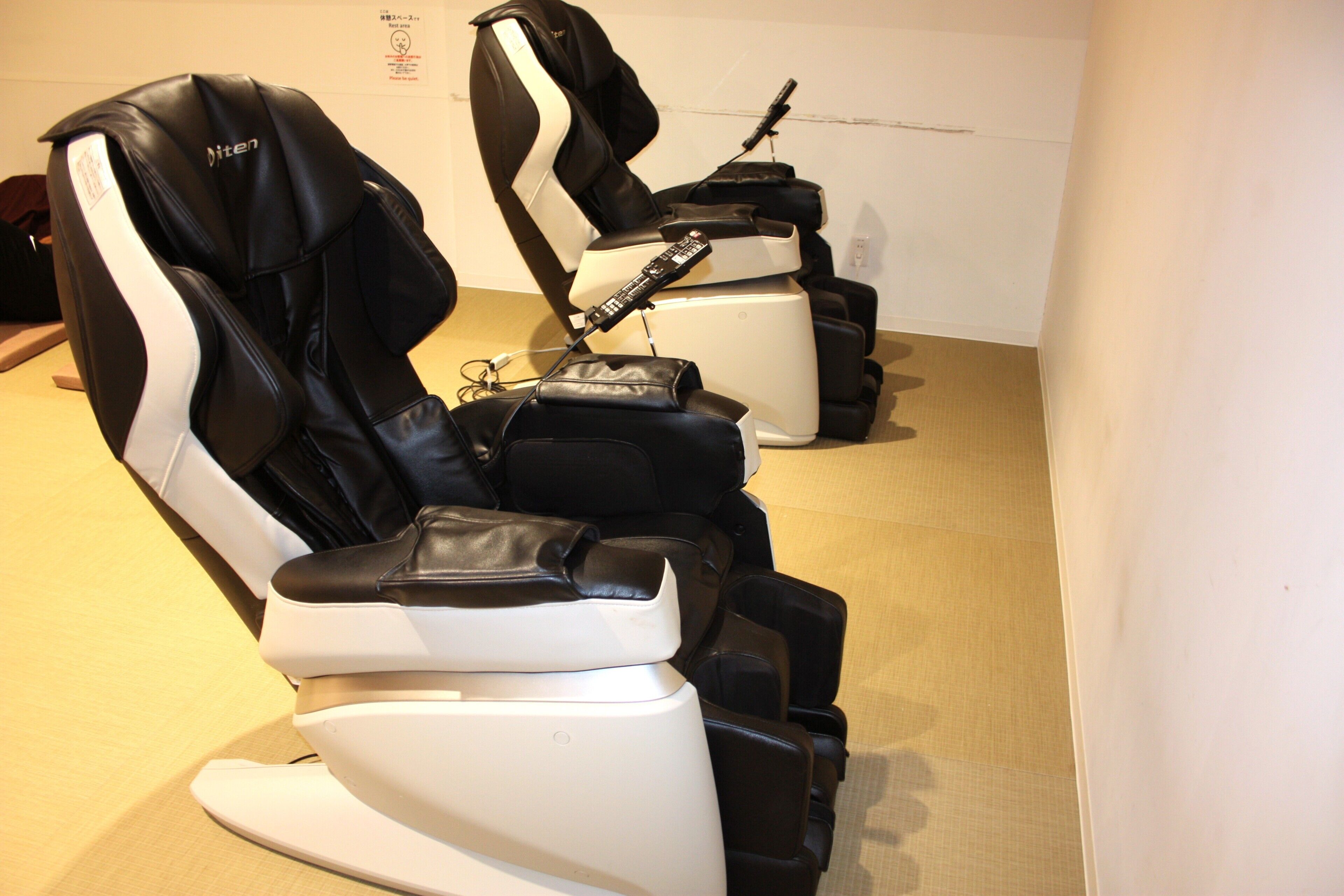 Una fila de sillones de masaje con controles remotos, ubicada en una habitación con pared lisa y piso alfombrado.
