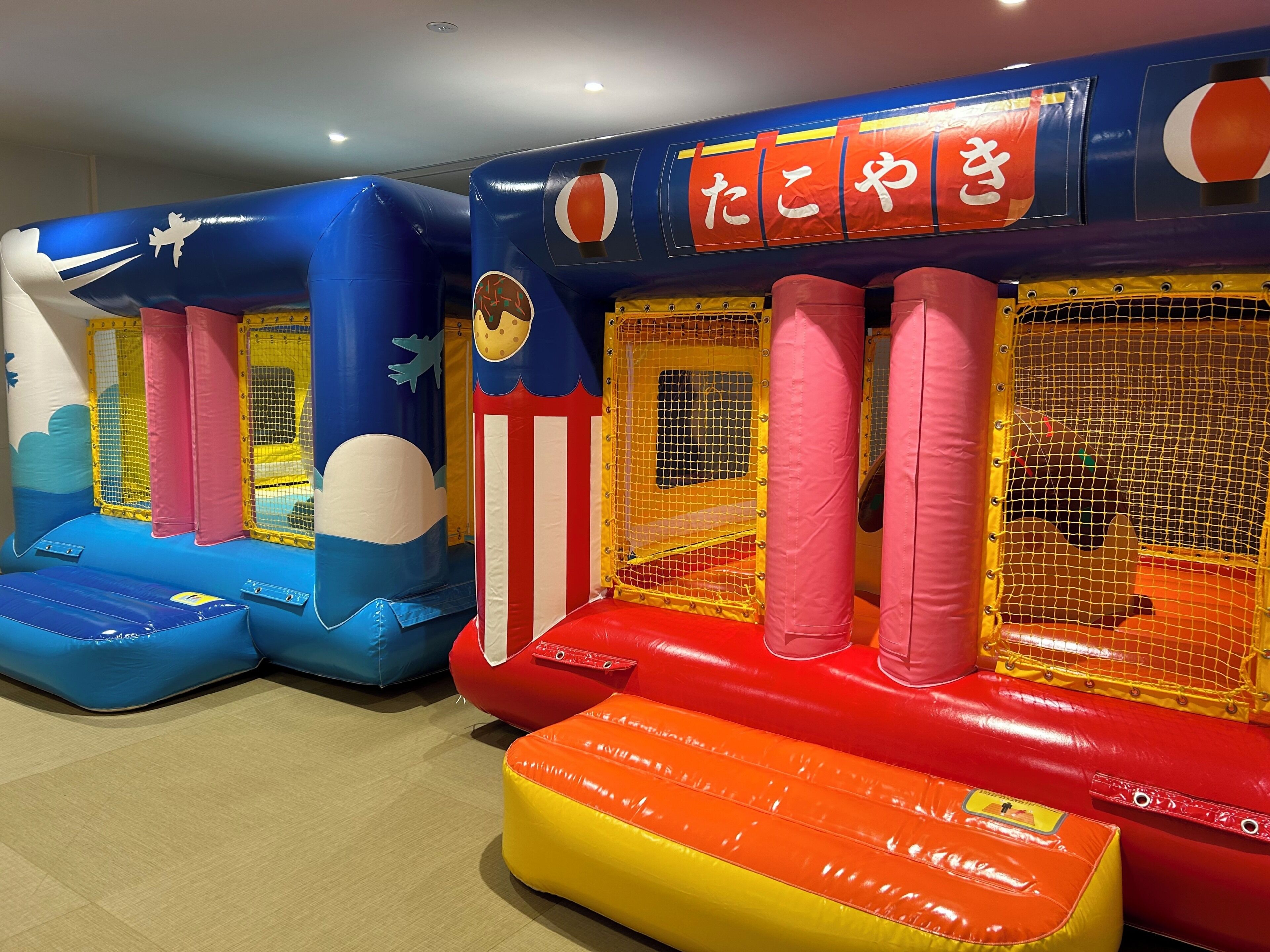 Un espace de jeux intérieur avec des structures gonflables et des zones de jeux délimitées par des filets.