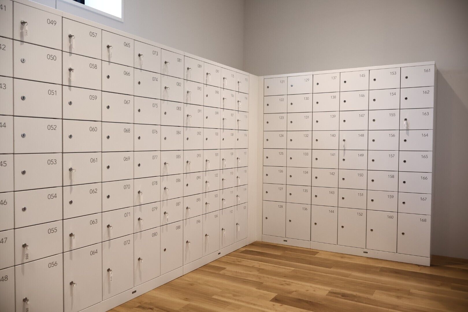 A row of white lockers with numbers on each, arranged in a room with wooden flooring.