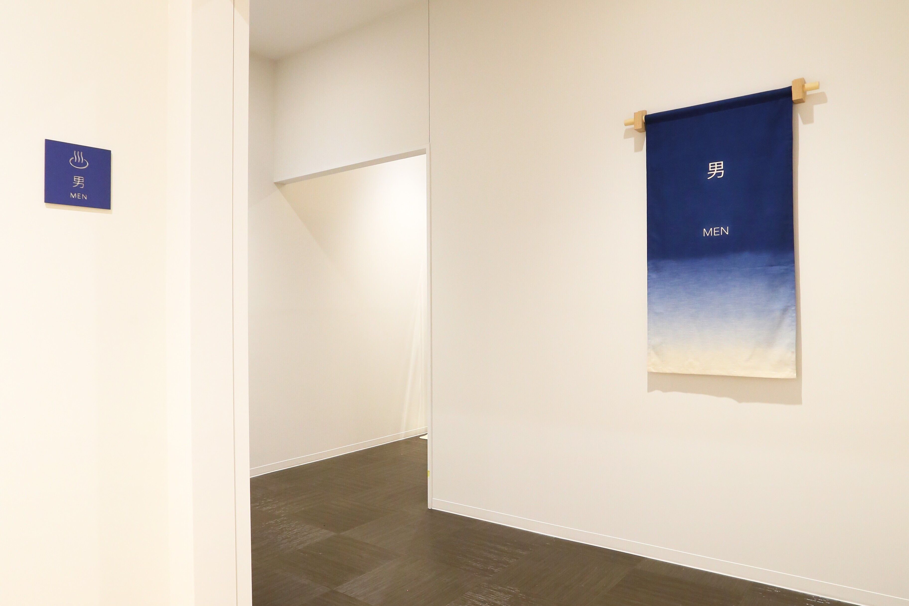 A hallway with a blue sign indicating a men's section, a wooden door, and a wall-mounted banner with text.