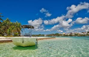 Ein Boot vor Anker in der Nähe eines Strandes mit klarem türkisblauem Wasser, Palmen und einer in der Ferne liegenden Stadt.