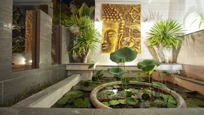 Un espace extérieur moderne agrémenté d’un élément aquatique, de plantes en pot et d’une grande statue de Bouddha.