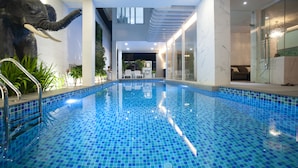 Une piscine intérieure aux murs recouverts de mosaïques bleues, avec une paroi en verre d’un côté et un aménagement intérieur moderne.