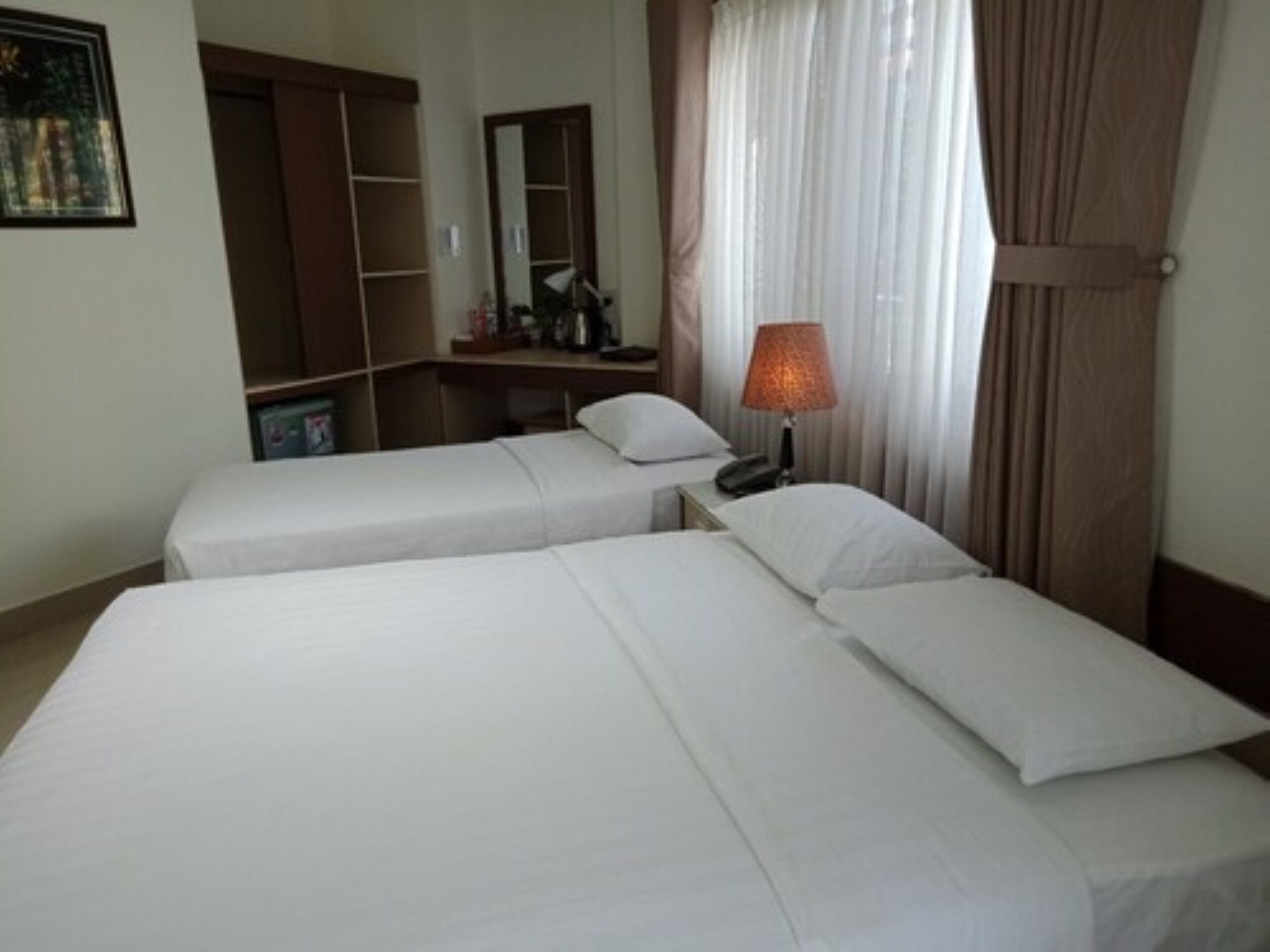 A hotel room with two single beds, a desk with a lamp, a mirror, and a wardrobe.