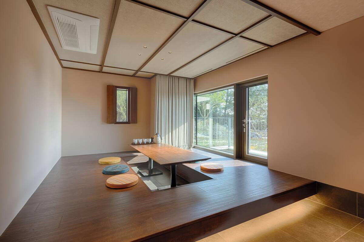 Ein modernes Zimmer mit einem Holzespeisetisch, einem Fenster mit Vorhängen und Blick auf Grün.
