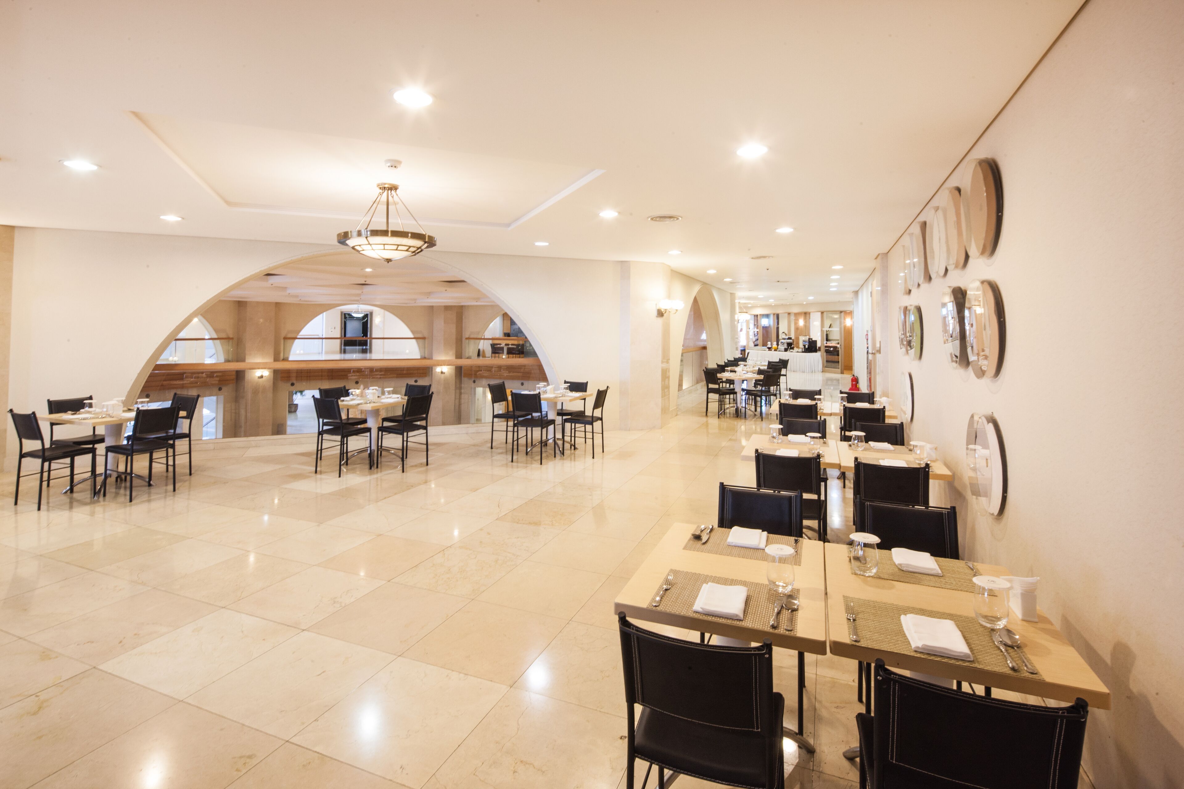 A spacious dining area with multiple tables and chairs, a chandelier, and a view of the kitchen in the background.