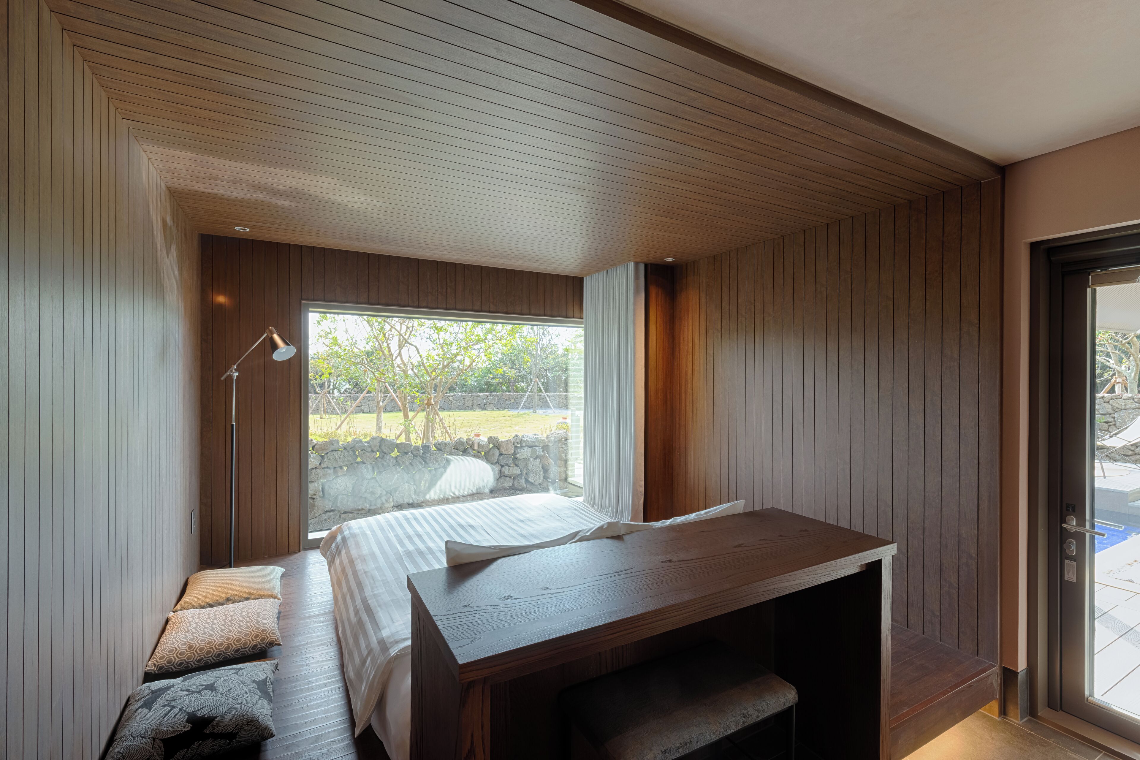 A modern bedroom with a wooden ceiling, a large window, a bed, and a desk.