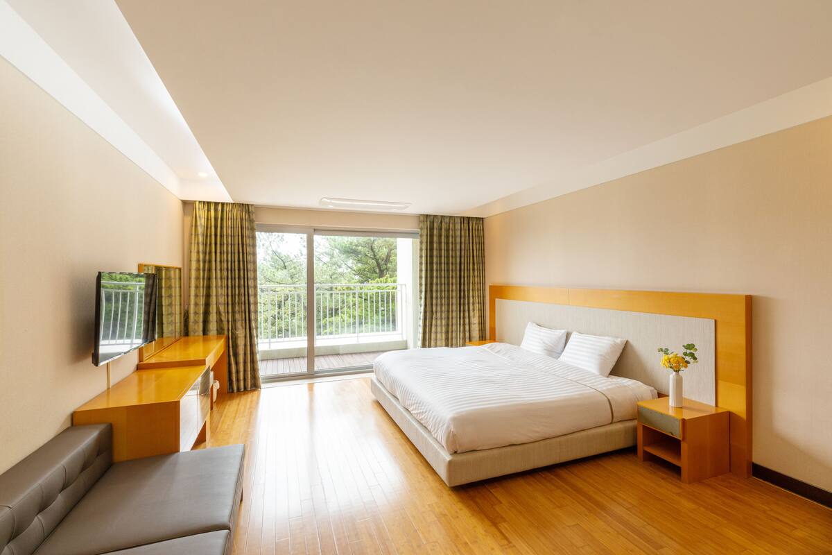 Ein Hotelzimmer mit Bett, Schreibtisch, Fernseher und einem Balkon mit Vorhängen.