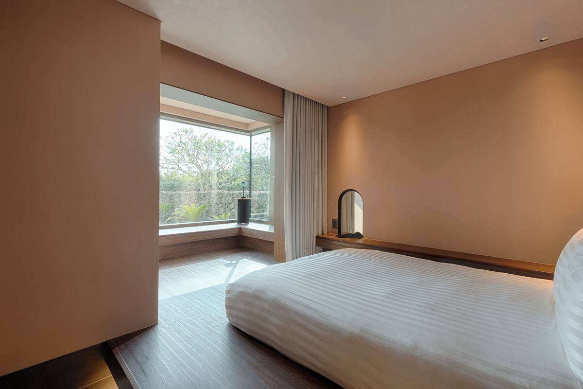 Ein modernes Hotelzimmer mit einem großen Bett, einem Nachttisch, einem Spiegel und einem Fenster mit Vorhängen.