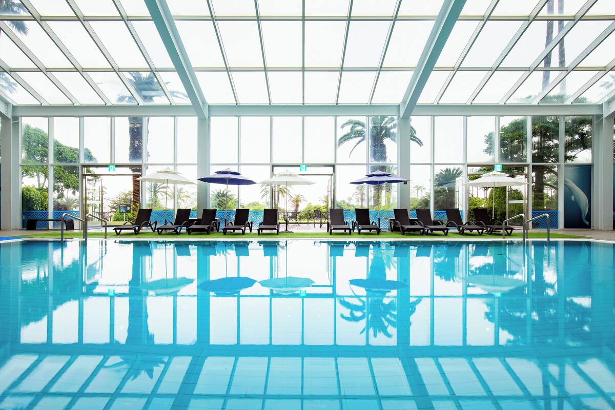 Ein Hallenbad mit Glasdächern, Sonnenschirmen und Liegestühlen.