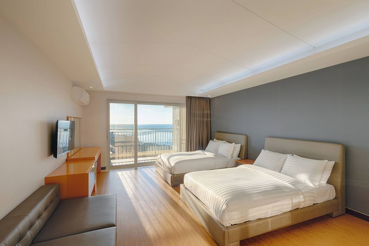 Ein Hotelzimmer mit zwei Betten, einer Sitzecke, einem Fernseher und einem Balkon mit Blick.