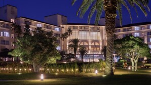 A multi-story hotel with balconies, a well-lit garden, and palm trees. - Sono Calm Jeju (Seogwipo)