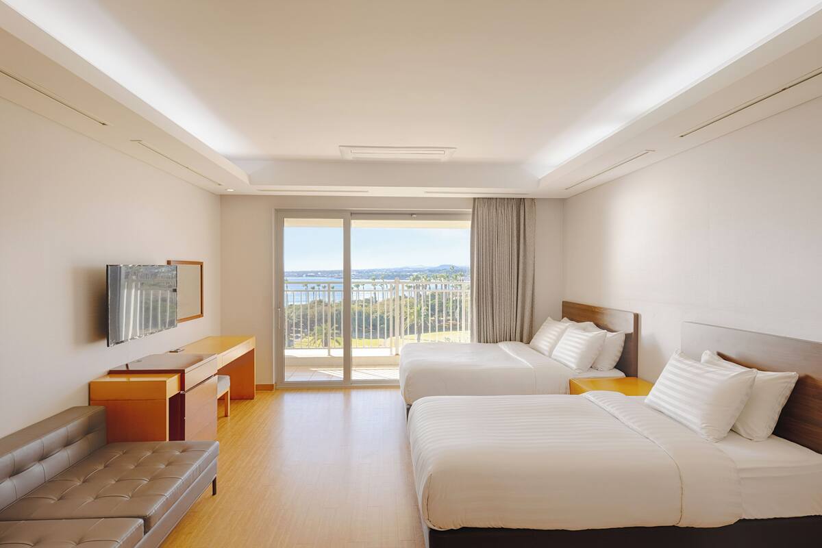 Ein Hotelzimmer mit zwei Betten, einem Sofa, einem Schreibtisch und einem großen Fenster mit Blick.
