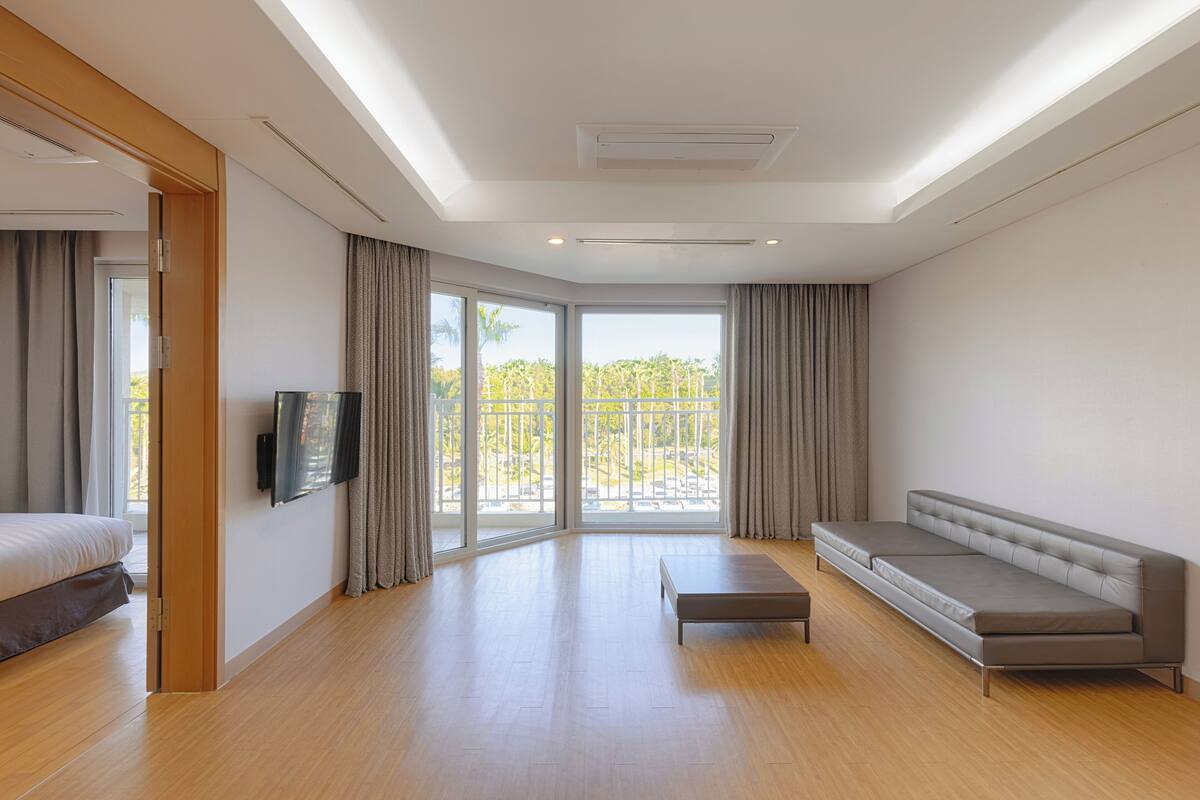 Ein modernes Hotelzimmer mit Bett, einer Sitzecke, einem Fernseher und einem Balkon mit Blick auf Palmen.