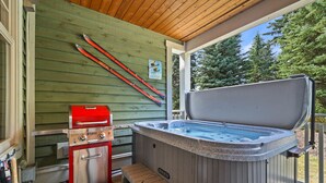 A covered outdoor area with a hot tub, a grill, and skis leaning against a wall. - Settler's Crossing #37 | True Ski-In/Ski-Out (Sun Peaks)