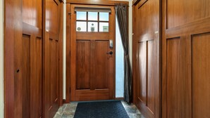 A wooden door with a window and a curtain, leading into a hallway with wooden walls. - Settler's Crossing #37 | True Ski-In/Ski-Out (Sun Peaks)