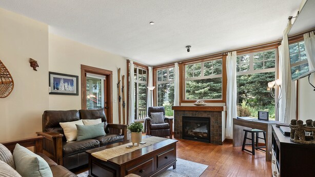 A cozy living room with a fireplace, leather sofa, and large windows. - Settler's Crossing #37 | True Ski-In/Ski-Out (Sun Peaks)