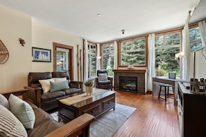 A cozy living room with a fireplace, leather sofa, and large windows. - Incredible ski in/ski out location SX# 37 (EV charger) (Sun Peaks)