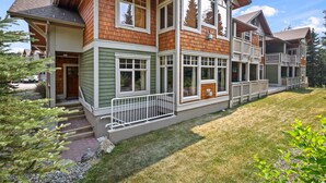 A two-story house with a front porch, large windows, and a well-maintained lawn. - Settler's Crossing #37 | True Ski-In/Ski-Out (Sun Peaks)