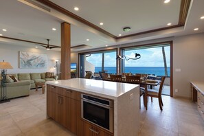 Een moderne keuken met een groot eiland, houten kastjes en uitzicht op de oceaan.