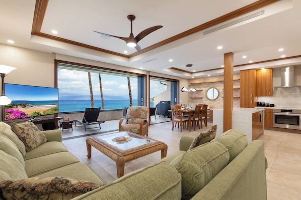 A spacious living area with a large window offering a view of the ocean, a ceiling fan, and a modern kitchen with wooden cabinets.