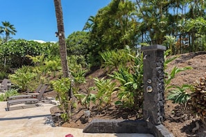 A landscaped outdoor area with a curved seating area, palm trees, and a stone pillar with a water feature.
