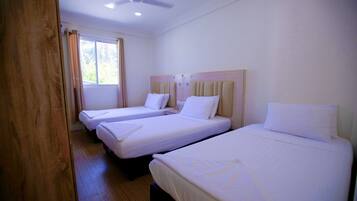 A hotel room with three single beds, a ceiling fan, and a window with curtains.