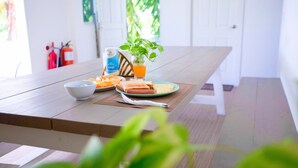 Une table de salle à manger en bois, avec un saladier, une assiette de nourriture, un verre de jus d’orange et une plante.