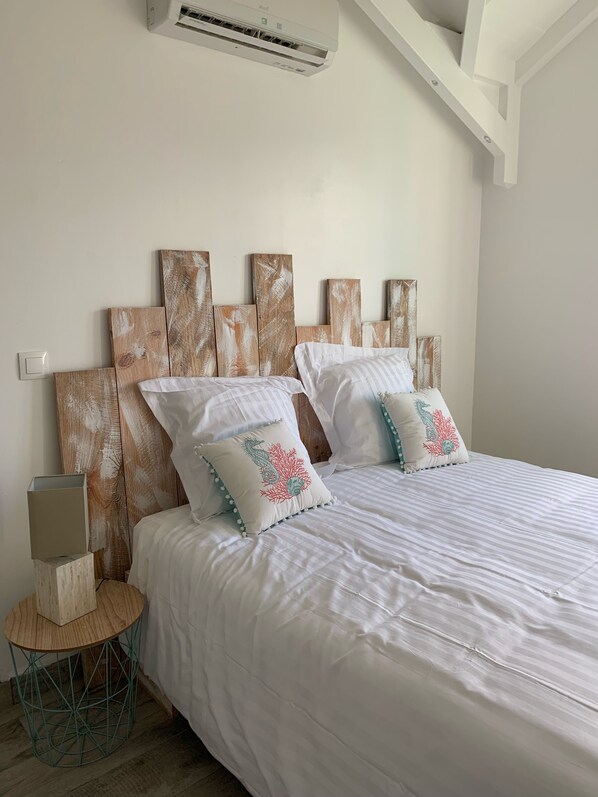 A bedroom with a bed, a nightstand, and a wall-mounted air conditioner. - Red coral, feet in the sand (Saint-François)