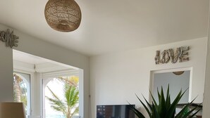 A modern living room with a large TV, a red patterned chair, a potted plant, and a 'LOVE' sign on the wall. - Red coral, feet in the sand (Saint-François)