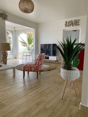 A modern living room with a large TV, a red patterned chair, a potted plant, and a 'LOVE' sign on the wall.